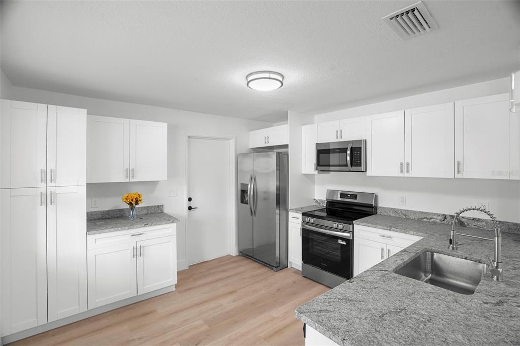 A modern kitchen features white cabinets, granite countertops, stainless steel appliances, and light wood flooring — 4406 W WALLACE AVENUE, TAMPA, FL