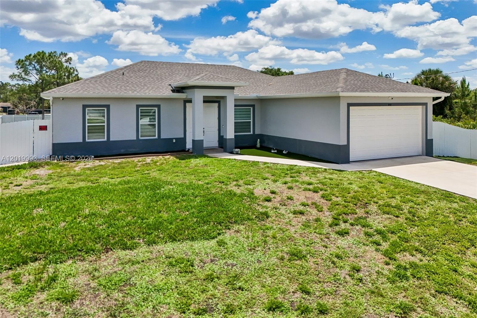 A single-story house with a gray exterior, a two-car garage, and a patchy lawn — 910 Richmond Ave N, Lehigh Acres FL 33972, LEHIGH ACRES, FL