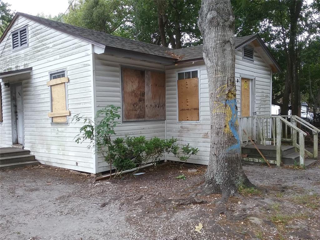A small, weathered white house with boarded-up windows and a tree in the front yard — 1815 NE 16TH WAY, GAINESVILLE, FL