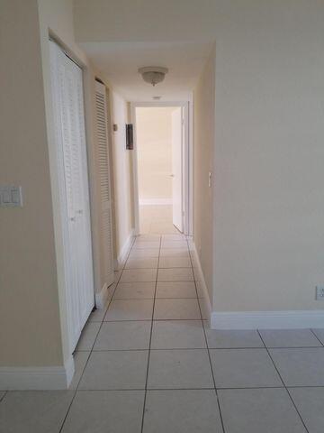 A hallway with white tile flooring leads to an open doorway in a neutral-toned interior — 720 N Dixie Highway # 202, Lantana FL 33462, LANTANA, FL