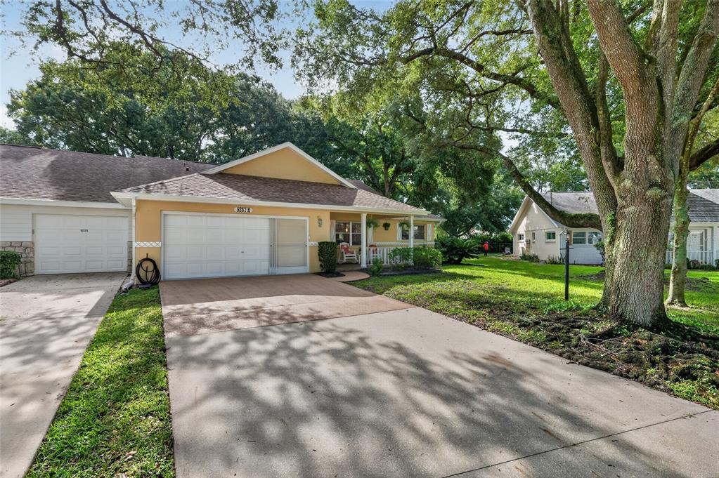 A yellow single-story house with a white garage door and a concrete driveway under trees — 9257 SW 82ND TERRACE UNIT H, OCALA, FL