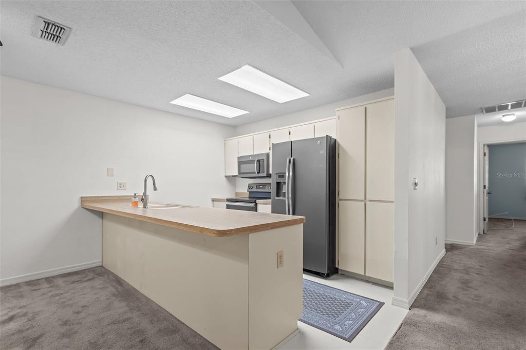 A kitchen features light-colored cabinets, a dark refrigerator, and a peninsula with a sink — 3416 CLAIRES COURT, NEW PORT RICHEY, FL