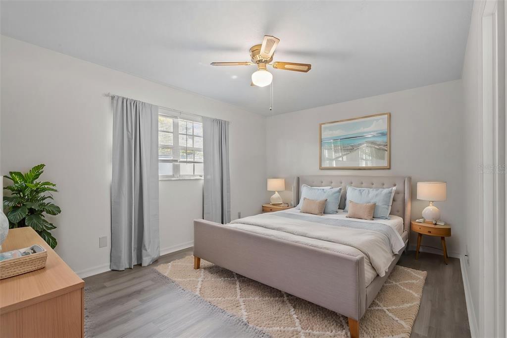 A bedroom features a gray upholstered bed, a ceiling fan, and light wood flooring — 3416 CLAIRES COURT, NEW PORT RICHEY, FL