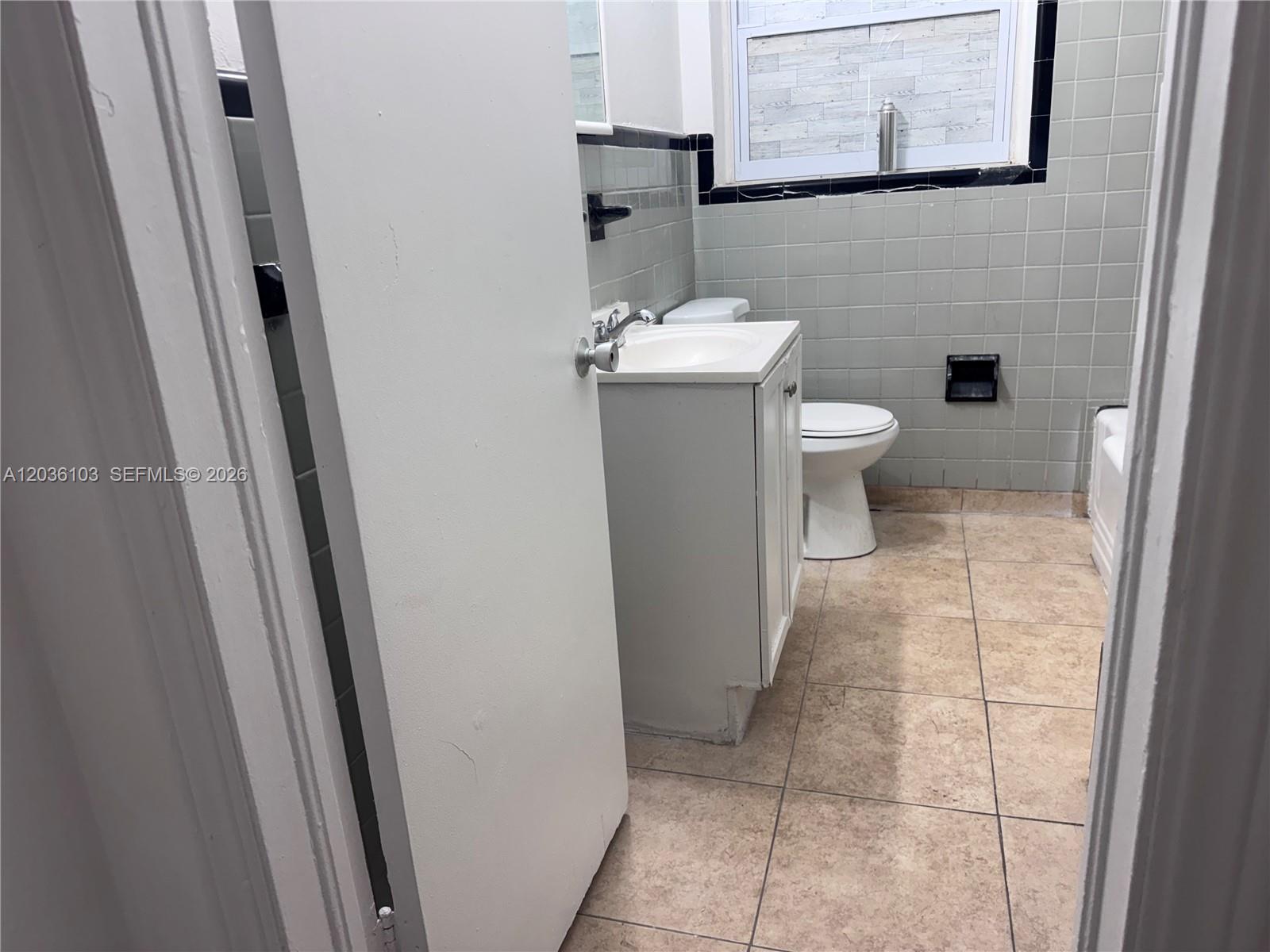 A bathroom features a white vanity, a toilet, and light gray tiled walls — 1238 NE 110th St # 1, Miami FL 33161, MIAMI, FL
