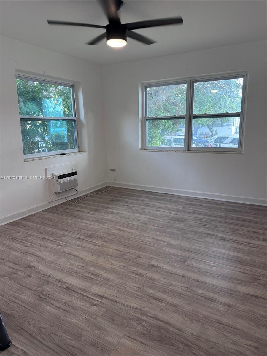 An empty room features light wood-look flooring, white walls, a ceiling fan, and window-mounted air conditioning — 1238 NE 110th St # 1, Miami FL 33161, MIAMI, FL