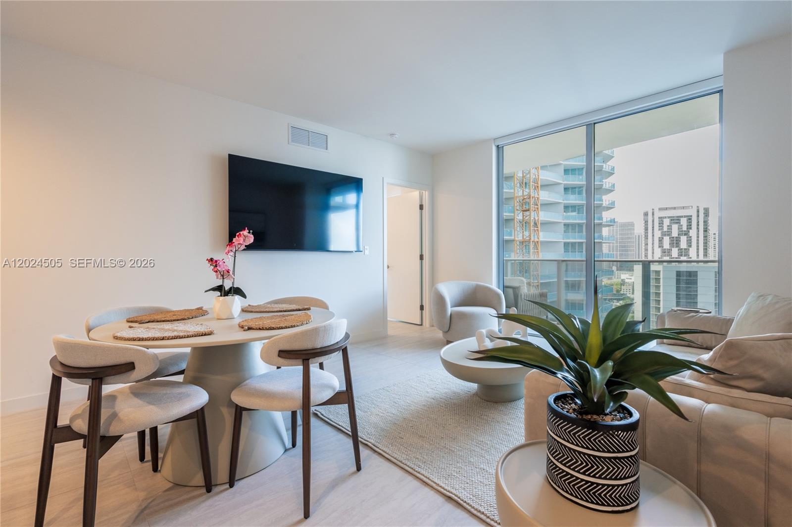 A modern living and dining area features a round table, sofa, and floor-to-ceiling windows — 77 SE 5TH STREET # 2602, Miami FL 33131, MIAMI, FL