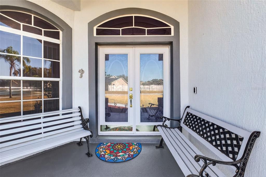 A covered entryway features two white benches, a colorful mat, and a double glass door — 365 VIA BIANCA DRIVE, DAVENPORT, FL