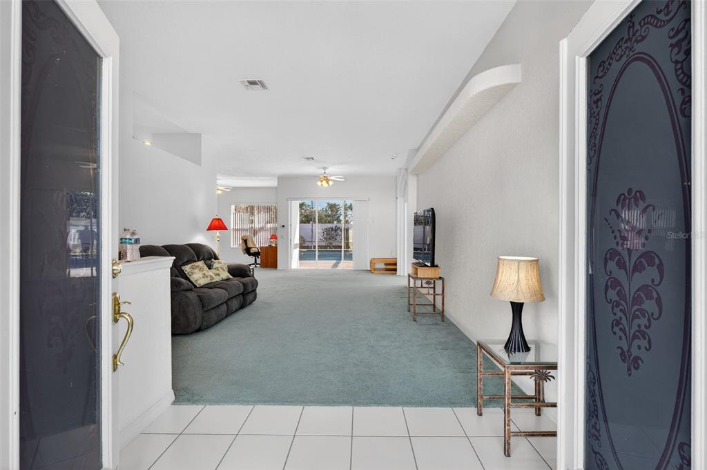An entryway with white tile floors leads into a carpeted living room with a pool view — 365 VIA BIANCA DRIVE, DAVENPORT, FL