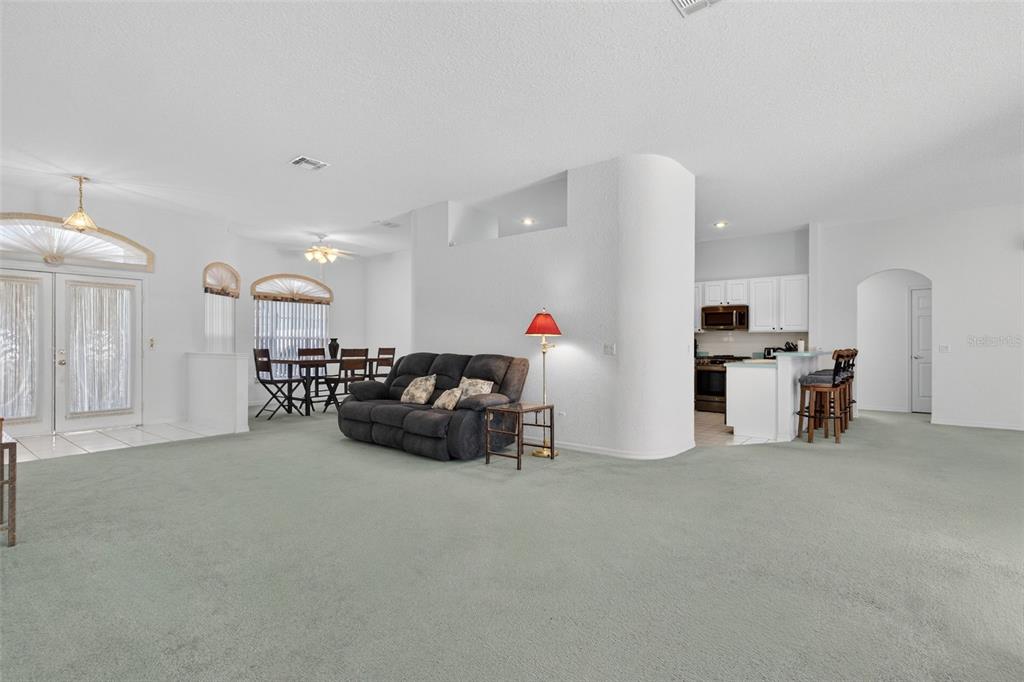A living room with light carpet, a dark sofa, and an adjacent dining area and kitchen — 365 VIA BIANCA DRIVE, DAVENPORT, FL