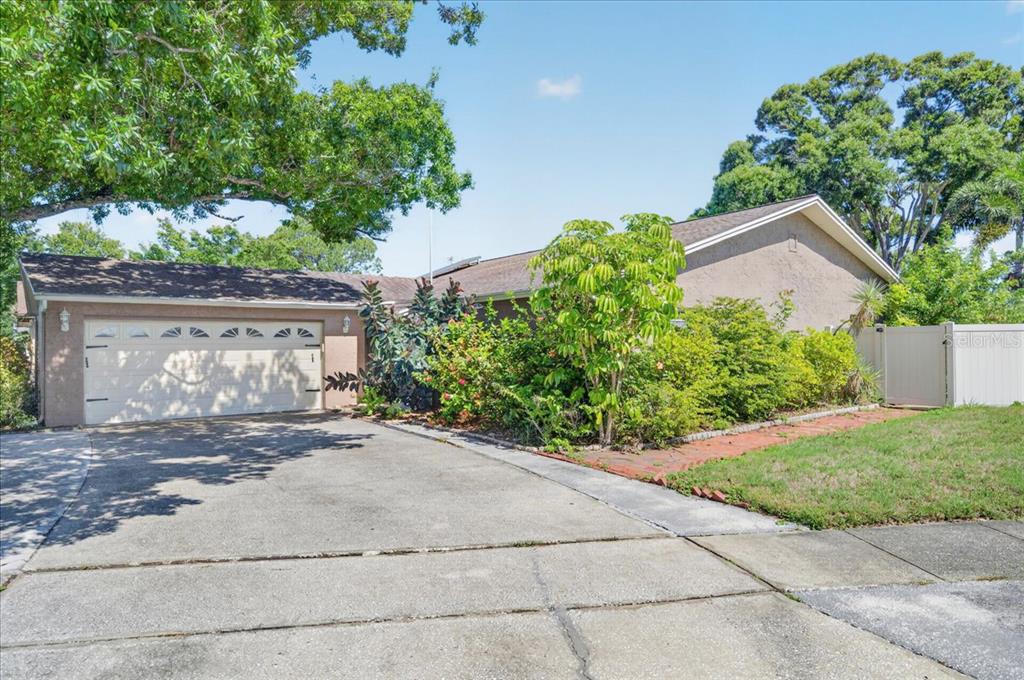 A single-story house with a beige stucco exterior, a two-car garage, and mature landscaping — 10202 56TH STREET N, PINELLAS PARK, FL