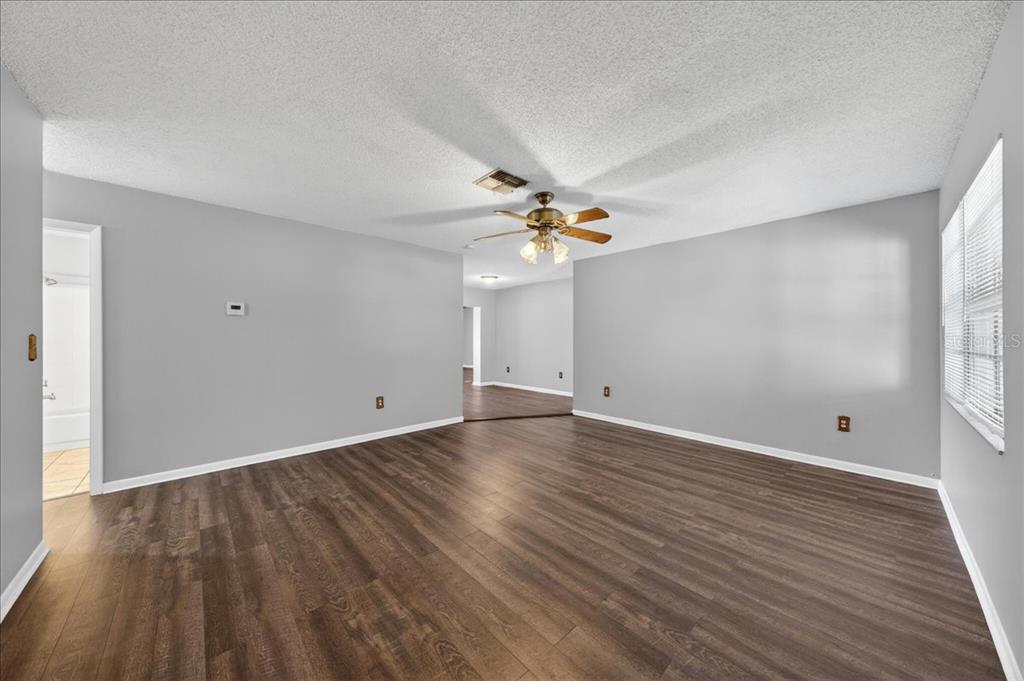 An empty living room with gray walls, dark wood-look flooring, and a ceiling fan — 10202 56TH STREET N, PINELLAS PARK, FL