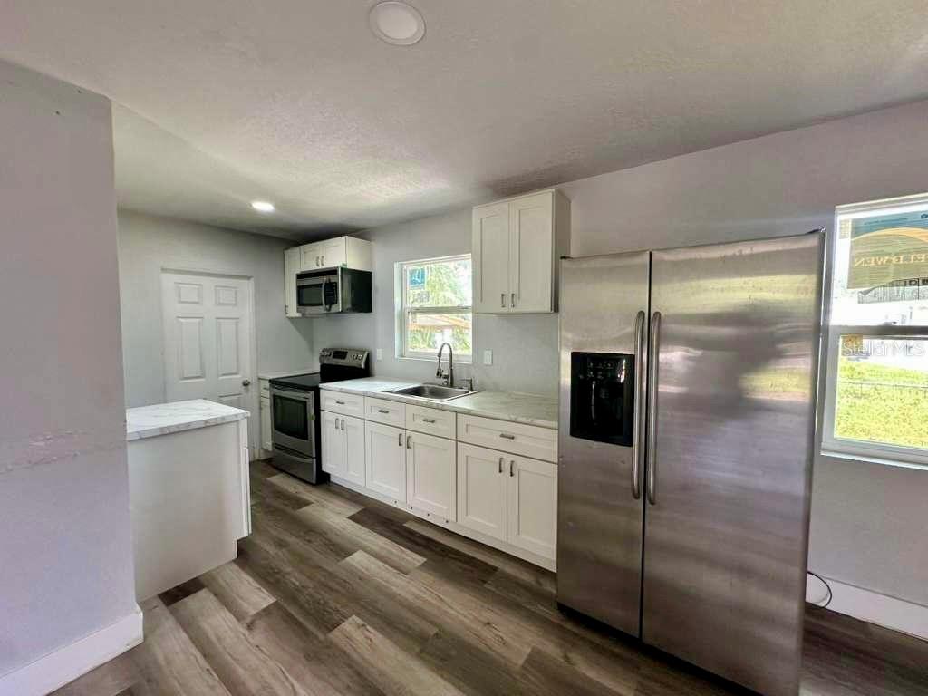 A kitchen with white cabinets, stainless steel appliances, and wood-look flooring — 1550 E BAY STREET, BARTOW, FL