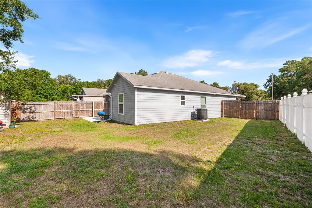 A backyard view of a gray single-story house with a wooden fence and lawn — 608 PINEVILLE LANE, LAKELAND, FL
