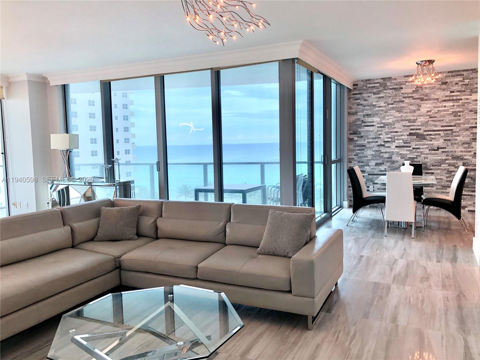 A modern living room features a large sectional sofa, glass tables, and floor-to-ceiling windows — 3101 S Ocean Dr # 801, Hollywood FL 33019, HOLLYWOOD, FL