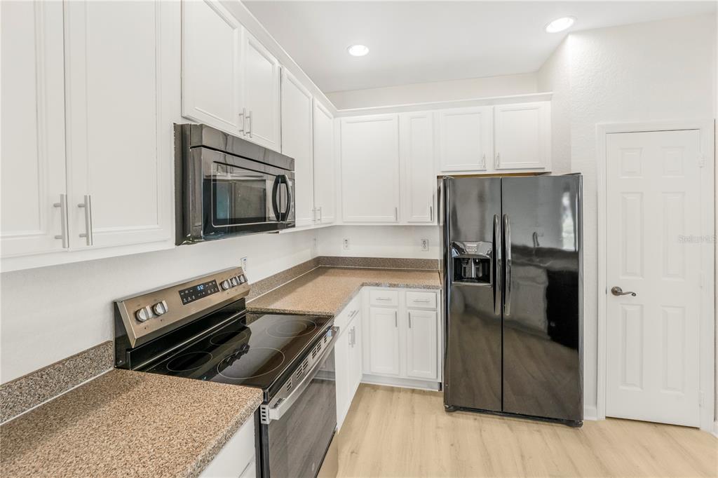 A kitchen features white cabinets, granite countertops, black appliances, and light wood-look flooring — 3351 WHITESTONE CIRCLE UNIT 304, KISSIMMEE, FL