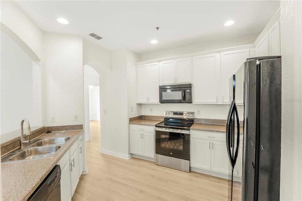 A kitchen features white cabinets, granite countertops, stainless steel appliances, and light wood-look flooring — 3351 WHITESTONE CIRCLE UNIT 304, KISSIMMEE, FL