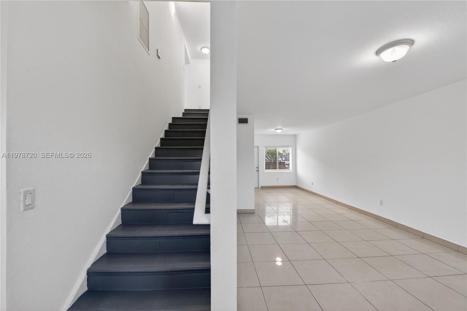 A staircase with dark steps sits beside a bright, tiled living area with white walls — 475 NW 84th Ter # 475, Miami FL 33150, MIAMI, FL