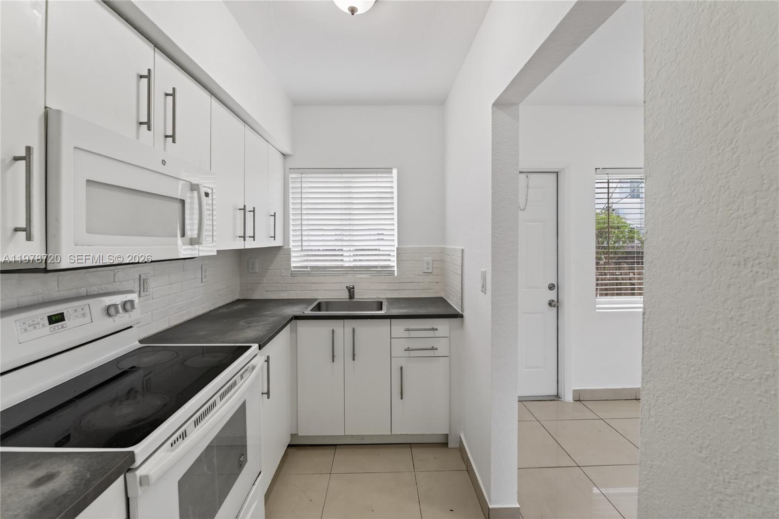 A white kitchen features dark countertops, a microwave, and tile flooring — 475 NW 84th Ter # 475, Miami FL 33150, MIAMI, FL