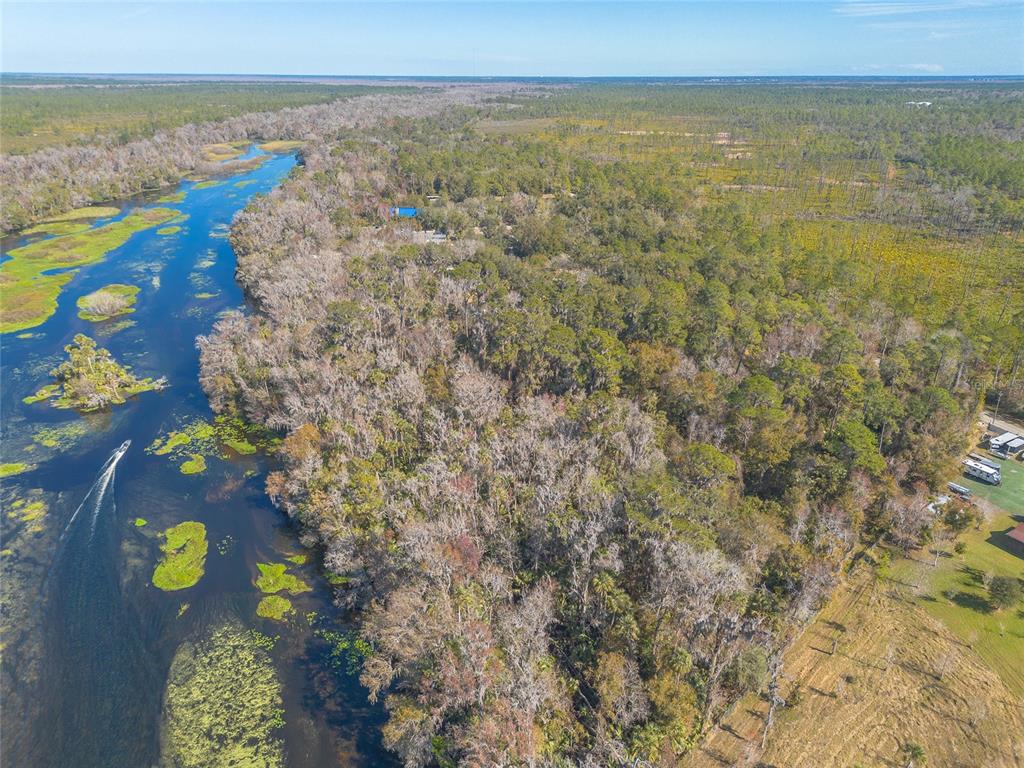 An aerial view shows a river flowing past a dense forest and a grassy field — 176 WEKIVA PARK DRIVE, SANFORD, FL