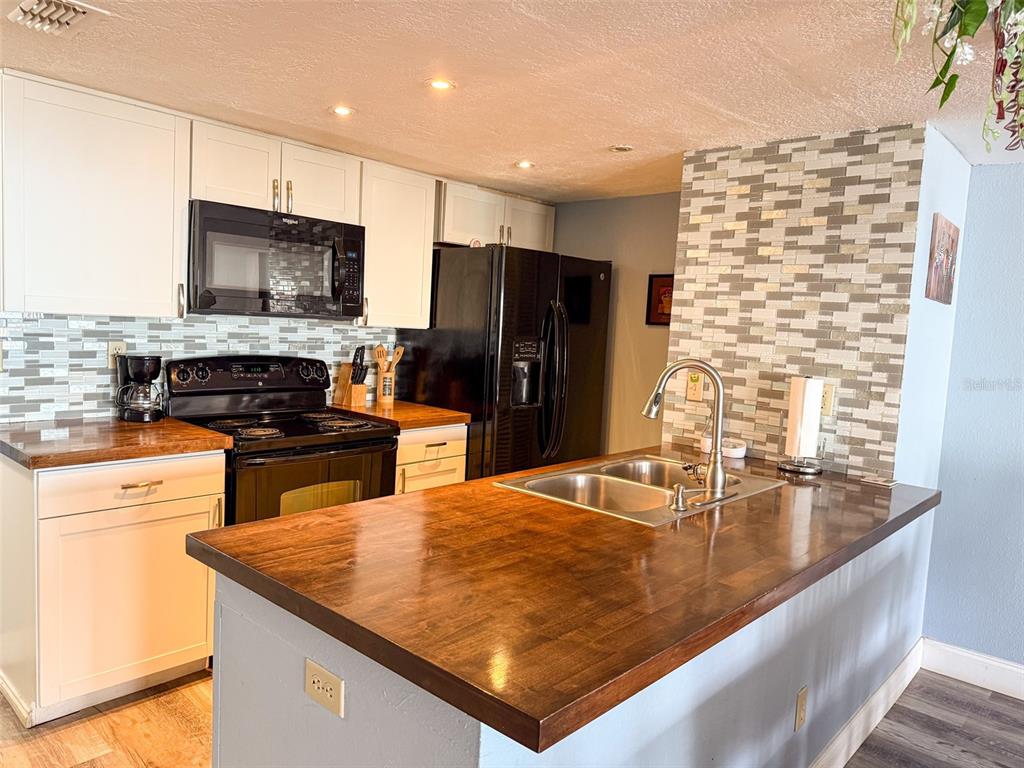 A kitchen features white cabinets, dark wood countertops, a black stove, and a tiled backsplash — 2731 N POINCIANA BOULEVARD UNIT 105, KISSIMMEE, FL