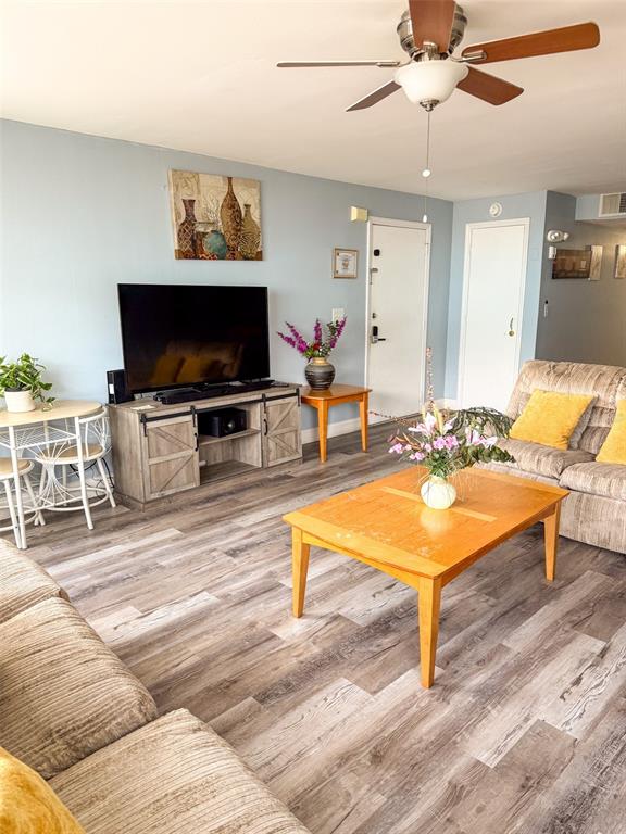 A living room features light blue walls, wood-look flooring, a television console, and a ceiling fan — 2731 N POINCIANA BOULEVARD UNIT 105, KISSIMMEE, FL