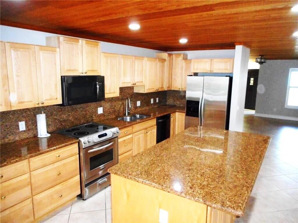 A kitchen features light wood cabinets, granite countertops, stainless steel appliances, and a wood ceiling — 1903 Robalo Drive, Vero Beach FL 32960, VERO BEACH, FL