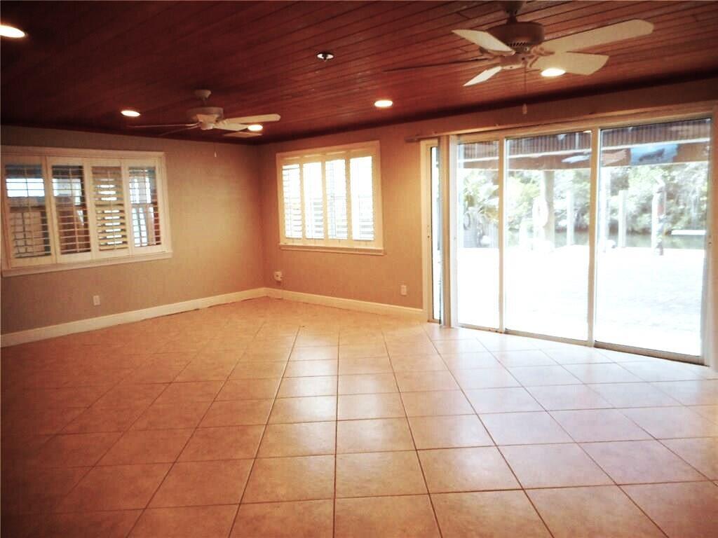 A spacious room with tile flooring, wood-paneled ceiling, ceiling fans, and sliding glass doors — 1903 Robalo Drive, Vero Beach FL 32960, VERO BEACH, FL