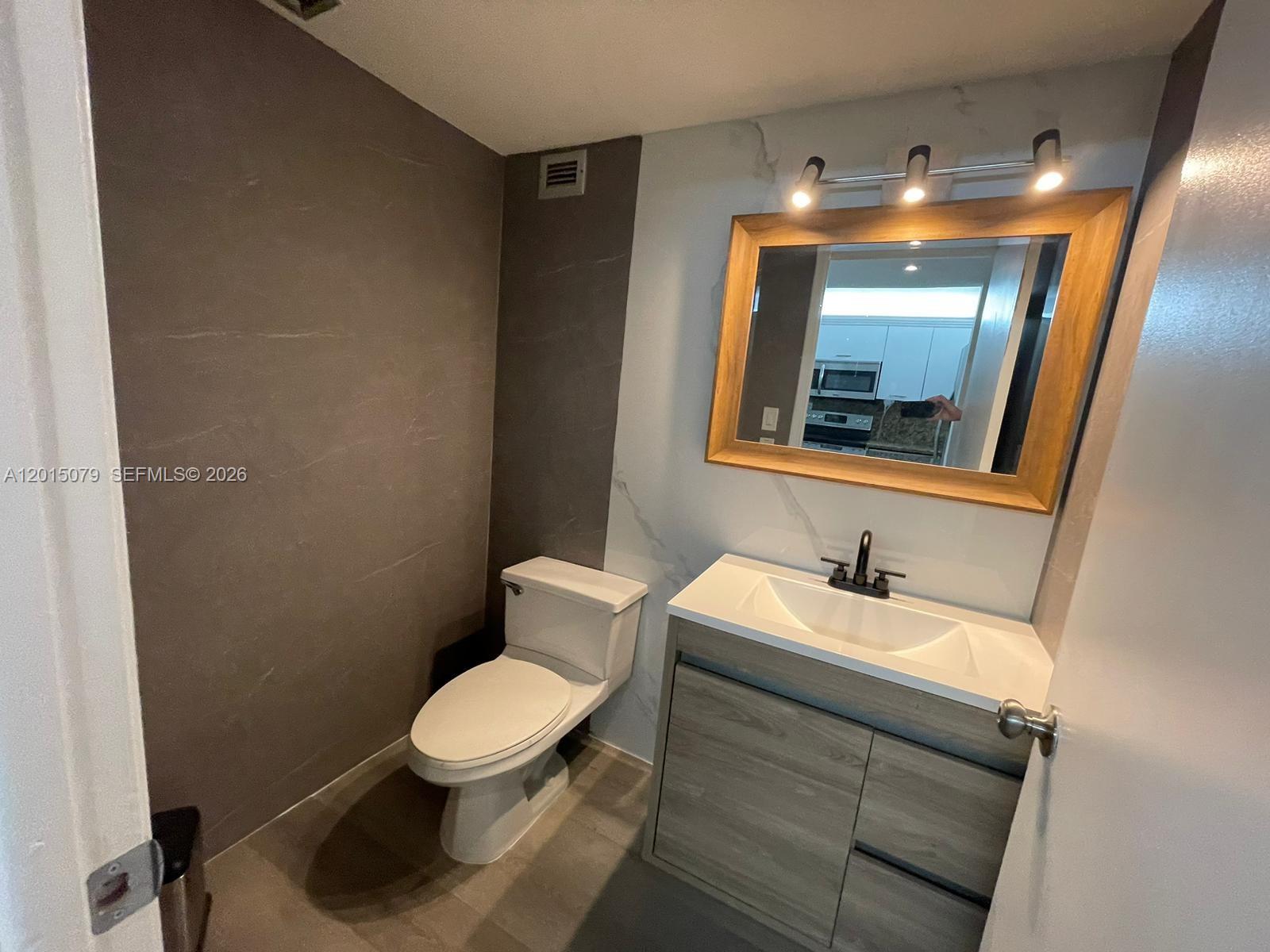 A bathroom features a wood-framed mirror, a modern vanity, and a toilet against tiled walls — 1901 Brickell Ave # B2104, Miami FL 33129, MIAMI, FL
