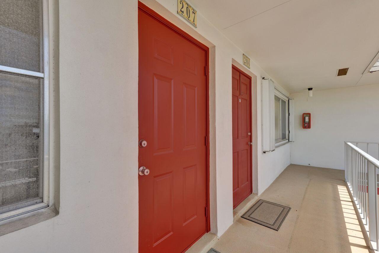 An exterior walkway features two red doors numbered 207 and 206 with beige walls — 3120 Cynthia Lane # 207, FL 33461, FL