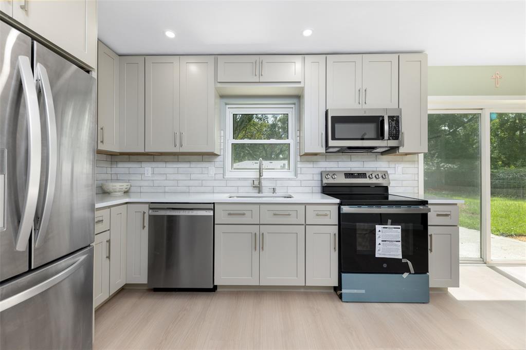 A kitchen features light gray cabinets, stainless steel appliances, white countertops, and a subway tile backsplash — 5621 NW 29TH TERRACE, GAINESVILLE, FL