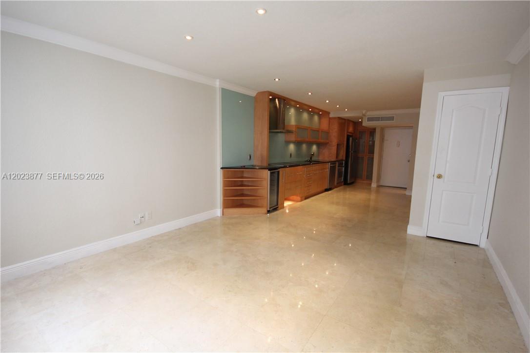 An open-concept kitchen with wood cabinetry and light tile flooring sits adjacent to a living area — 5401 Collins Ave # 339, Miami Beach FL 33140, MIAMI BEACH, FL