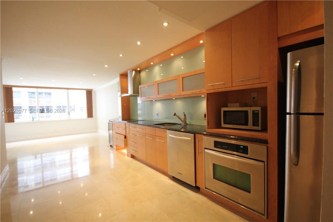A modern kitchen features light wood cabinetry, stainless steel appliances, and polished tile flooring — 5401 Collins Ave # 339, Miami Beach FL 33140, MIAMI BEACH, FL