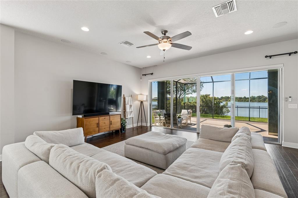 A living room features a large sectional sofa, a television on a wooden console, and sliding glass doors — 7223 HOURGLASS DRIVE, APOLLO BEACH, FL