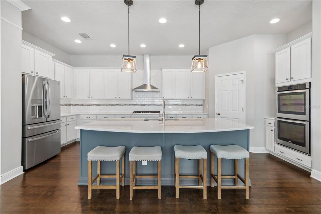 A kitchen features white cabinetry, a blue island with four stools, and stainless steel appliances — 7223 HOURGLASS DRIVE, APOLLO BEACH, FL
