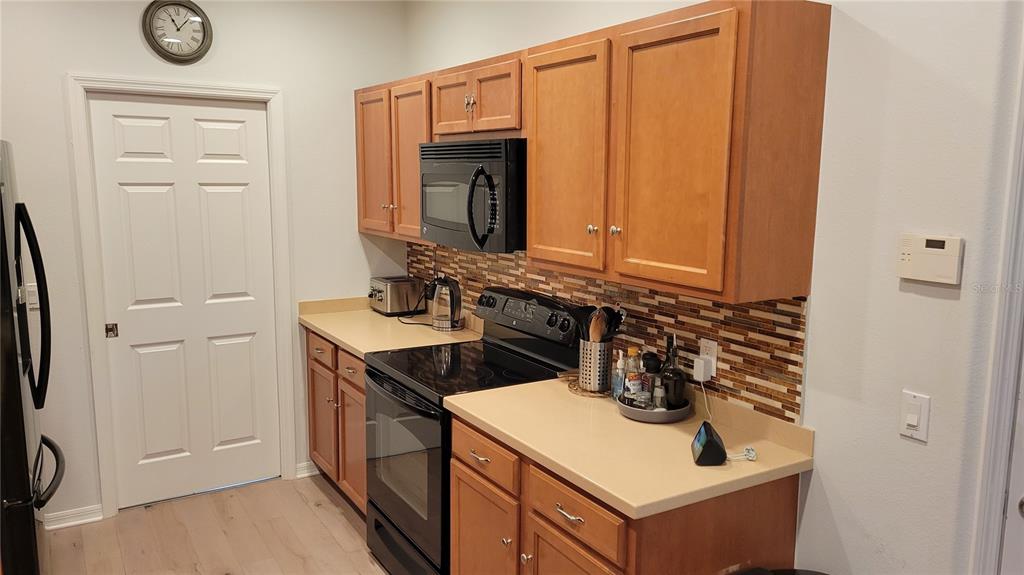 A kitchen features light wood cabinets, black appliances, a beige countertop, and a tiled backsplash — 3716 82ND AVENUE CIRCLE E UNIT 101, SARASOTA, FL