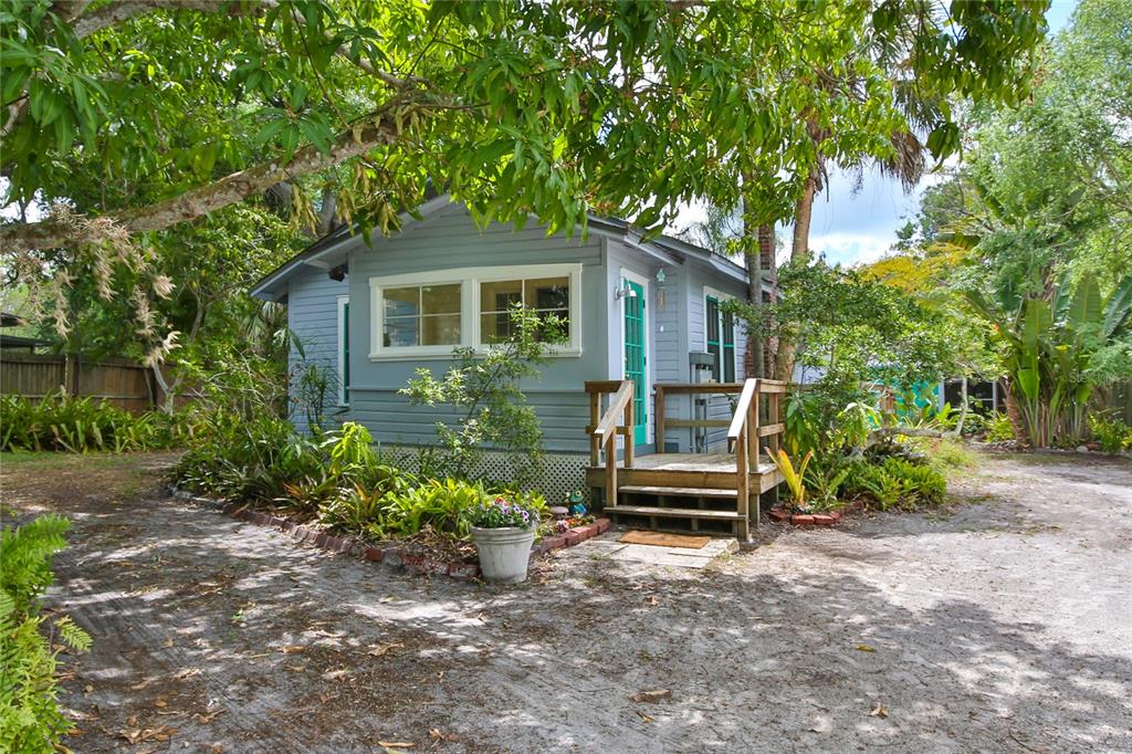 A small, light blue cottage with a wooden deck sits on a sandy, tree-shaded lot — 708 42ND STREET, SARASOTA, FL
