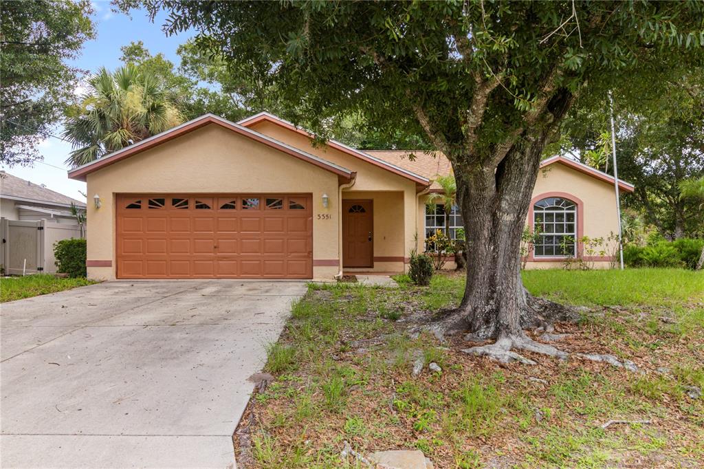 A single-story house with a tan stucco exterior, a brown garage door, and a large tree — 3351 TUCSON ROAD, NORTH PORT, FL