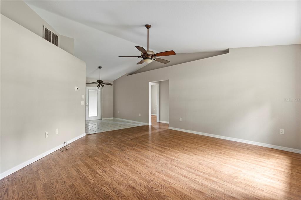 An empty living room features vaulted ceilings, wood-look flooring, and two ceiling fans — 3351 TUCSON ROAD, NORTH PORT, FL