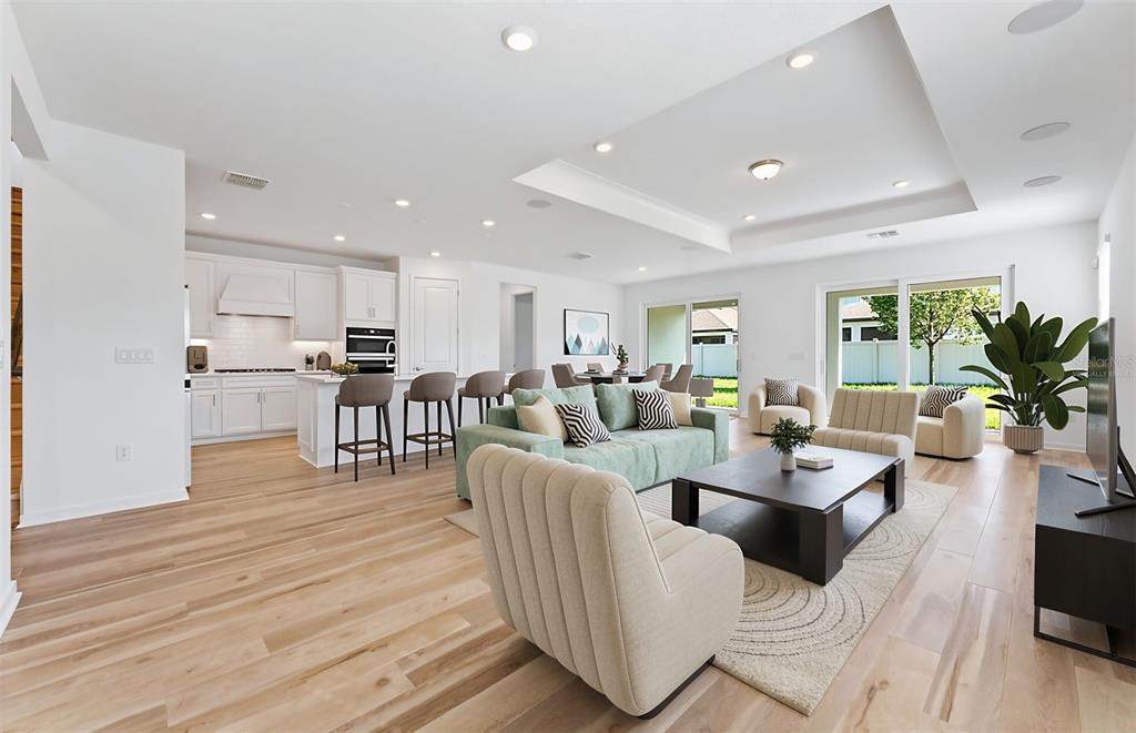 An open-concept living room and kitchen featuring light wood floors, white cabinetry, and modern furniture — 13630 BROOKSIDE HAVEN STREET, RIVERVIEW, FL