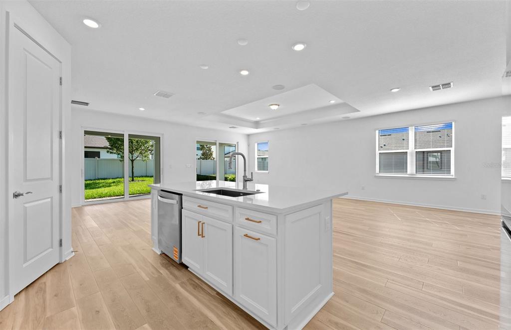A bright kitchen island with a sink and dishwasher sits in an open-concept living space — 13630 BROOKSIDE HAVEN STREET, RIVERVIEW, FL