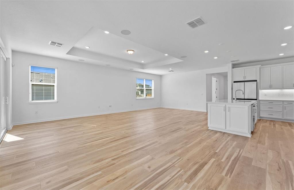 An open-concept living area features light wood flooring, white walls, and a tray ceiling — 13630 BROOKSIDE HAVEN STREET, RIVERVIEW, FL
