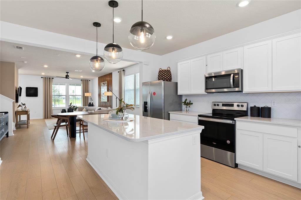 A modern kitchen features white cabinetry, a quartz-topped island, and pendant lighting over wood floors — 4596 ORCHARD VIEW ALLEY, CLERMONT, FL