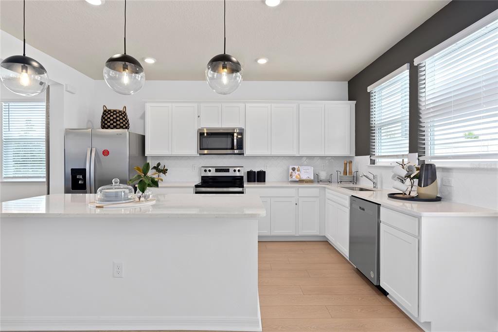 A modern kitchen features white cabinetry, stainless steel appliances, a large island, and pendant lighting — 4596 ORCHARD VIEW ALLEY, CLERMONT, FL
