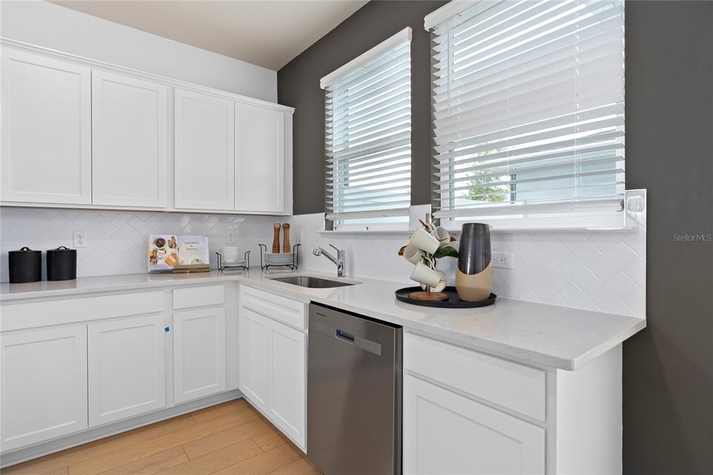 A kitchen features white cabinets, light countertops, a stainless steel dishwasher, and a herringbone backsplash — 4596 ORCHARD VIEW ALLEY, CLERMONT, FL