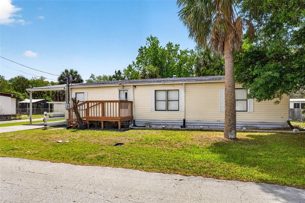 A single-story manufactured home with light yellow siding, a wooden deck, and a palm tree — 8552 W PEACOCK COURT, HOMOSASSA, FL