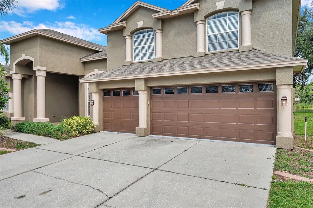 A two-story house exterior features a three-car garage, beige stucco walls, and white columns — 4812 WALNUT RIDGE ROAD, LAND O LAKES, FL