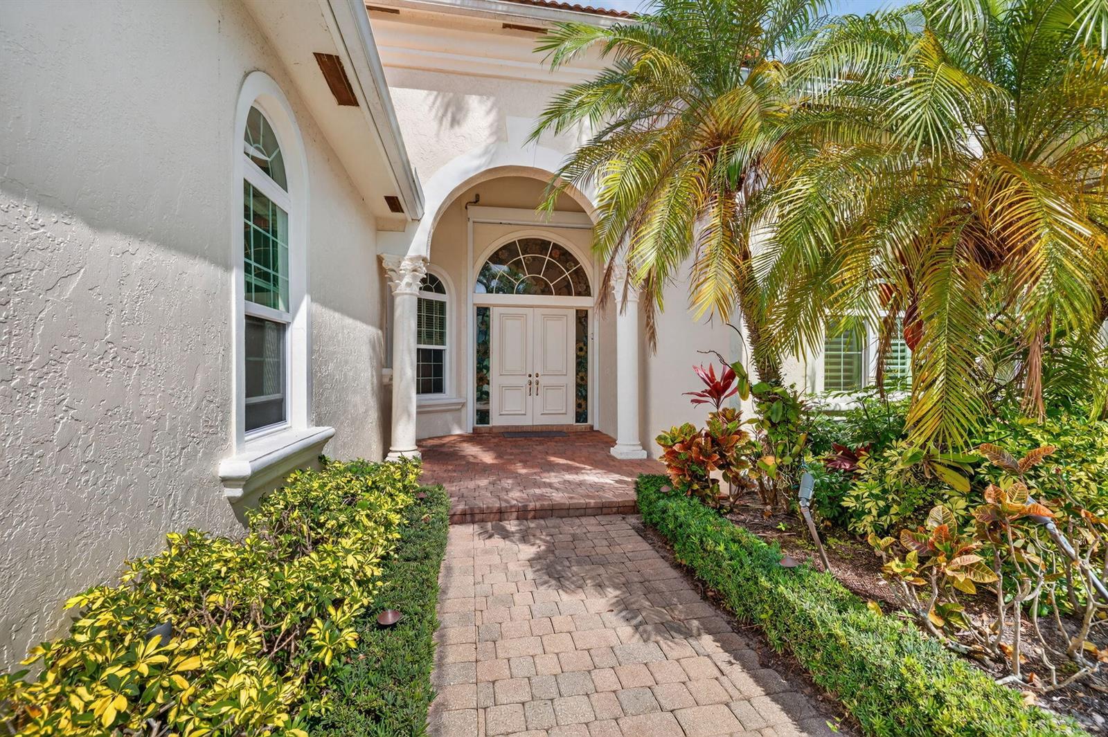 A brick walkway leads to the arched entryway of a house with white stucco walls — 6629 Grande Orchid Way, Delray Beach FL 33446, DELRAY BEACH, FL