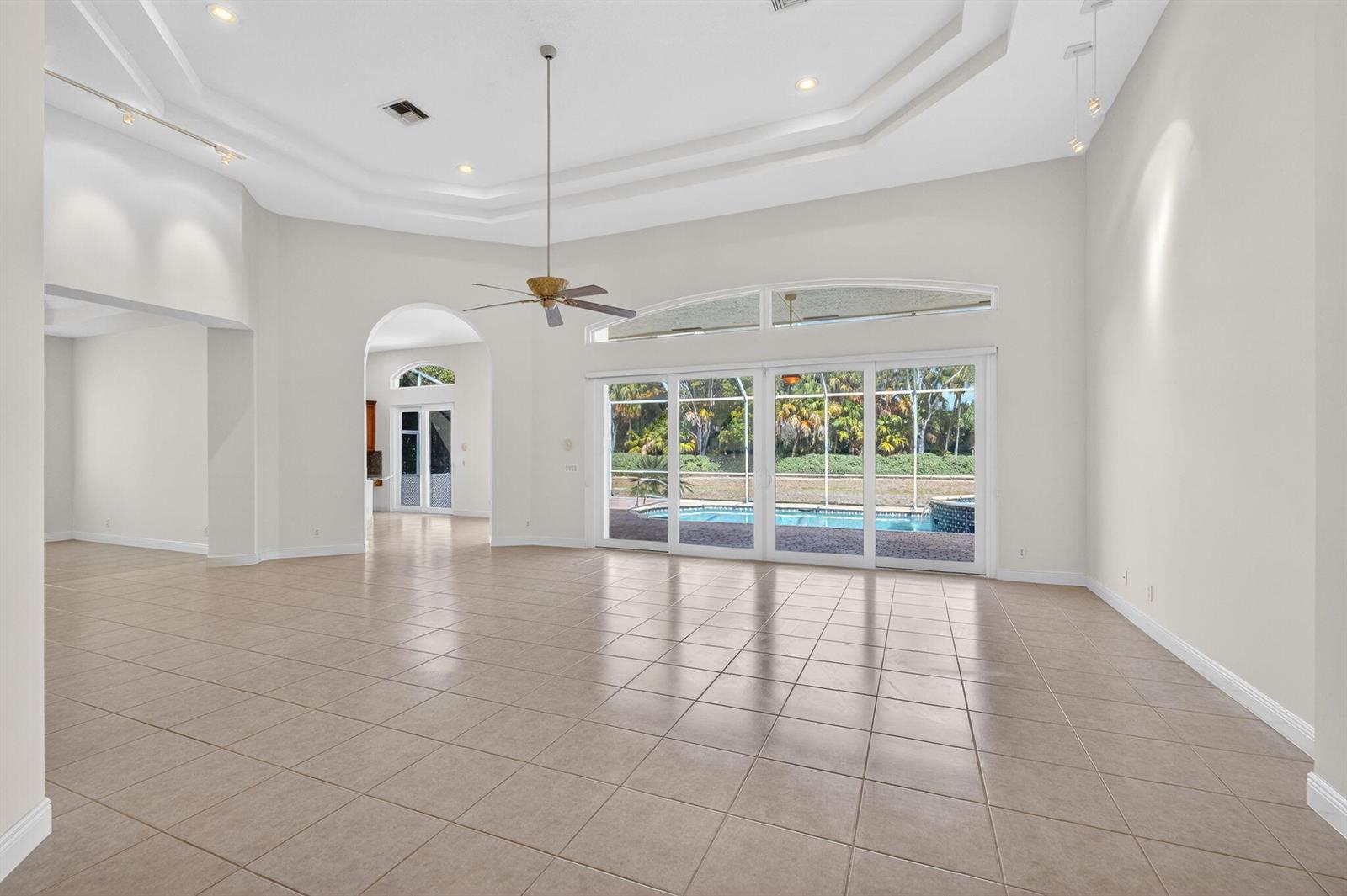 A spacious living room features tile flooring, a tray ceiling, and sliding glass doors to a pool — 6629 Grande Orchid Way, Delray Beach FL 33446, DELRAY BEACH, FL