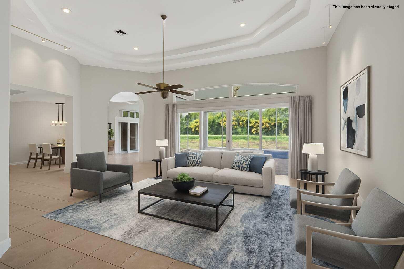 This virtually staged living room features a tray ceiling, tile flooring, and large sliding glass doors — 6629 Grande Orchid Way, Delray Beach FL 33446, DELRAY BEACH, FL