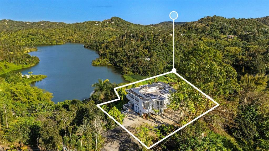 An aerial view shows a white multi-story house situated near a lake and lush forest — Carretera 742 Km.2.3 SECTOR LAS VILLAS BO. CARITE UNIT F2-F3, GUAYAMA, PR